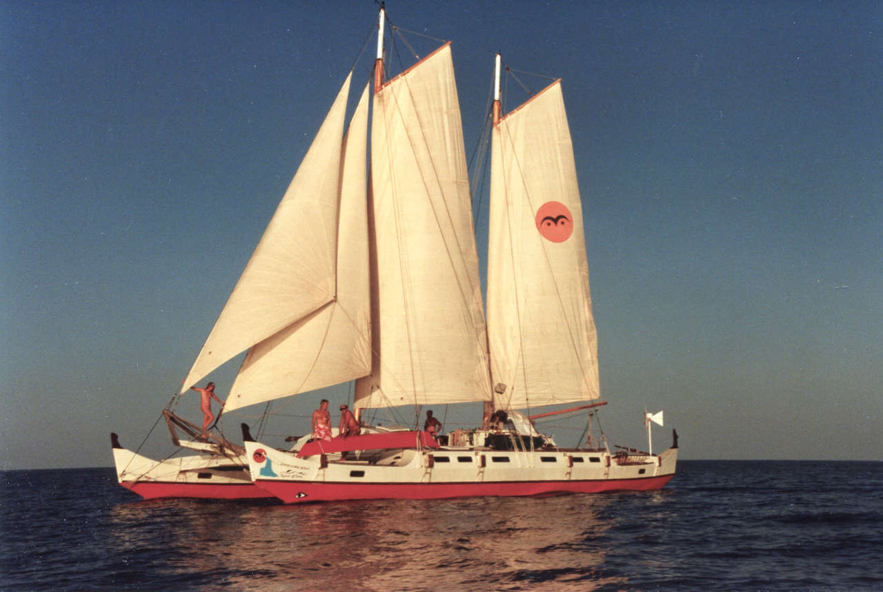 Large double sailing canoe, all sails up, sunny, people aboard