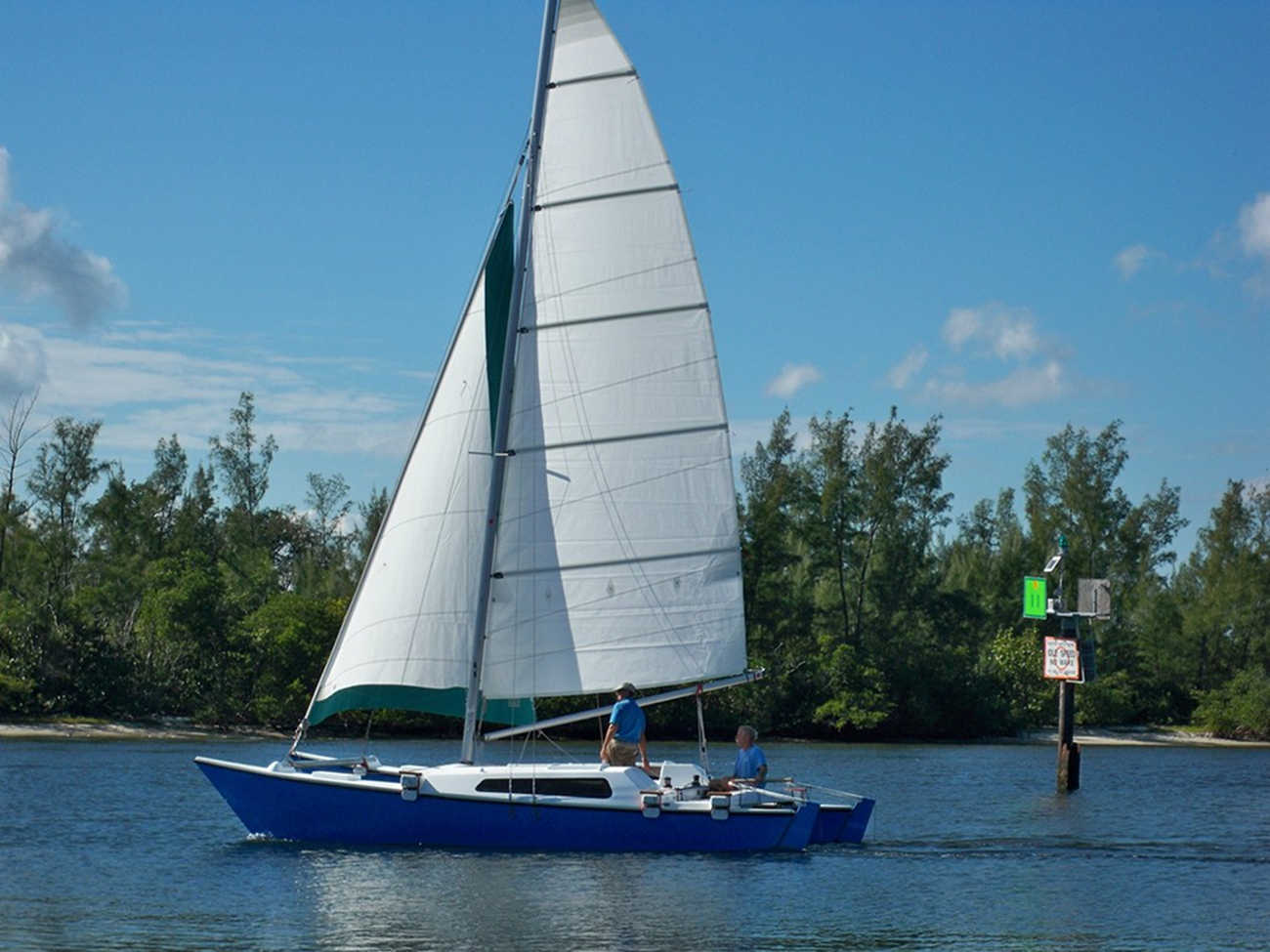 Blue Tiki 8m sailed by two people, trees in background