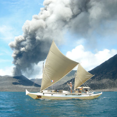 A catamaran sailing past a smoking volcano