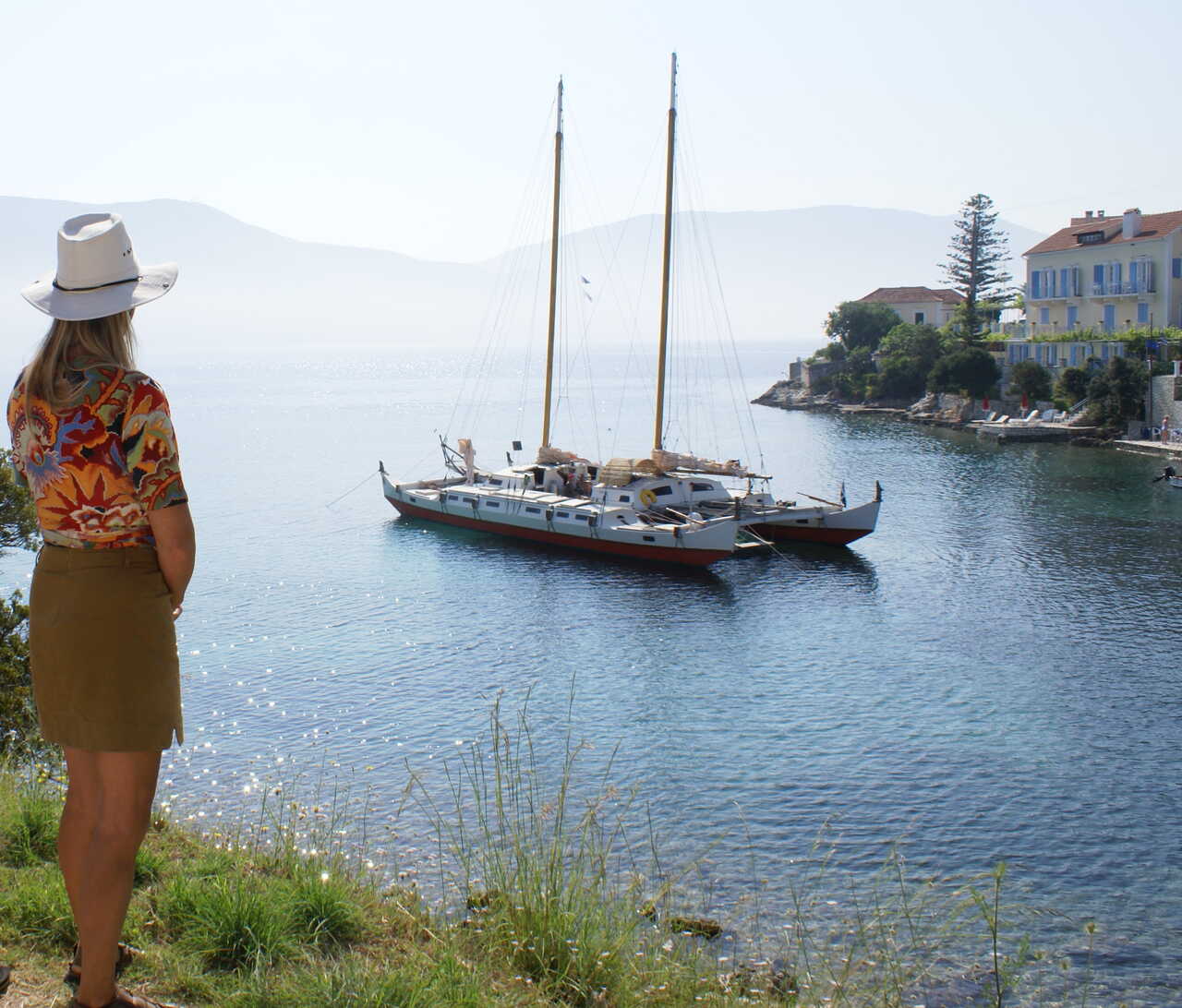 A woman looking out into a bay with a large catamaran at anchor