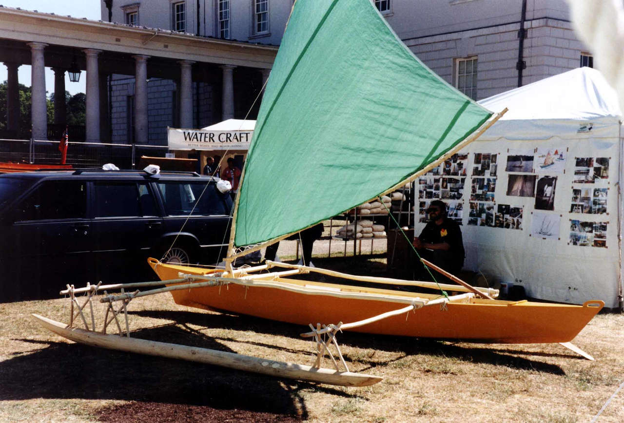 Outrigger canoe with yellow hull and green sail on land
