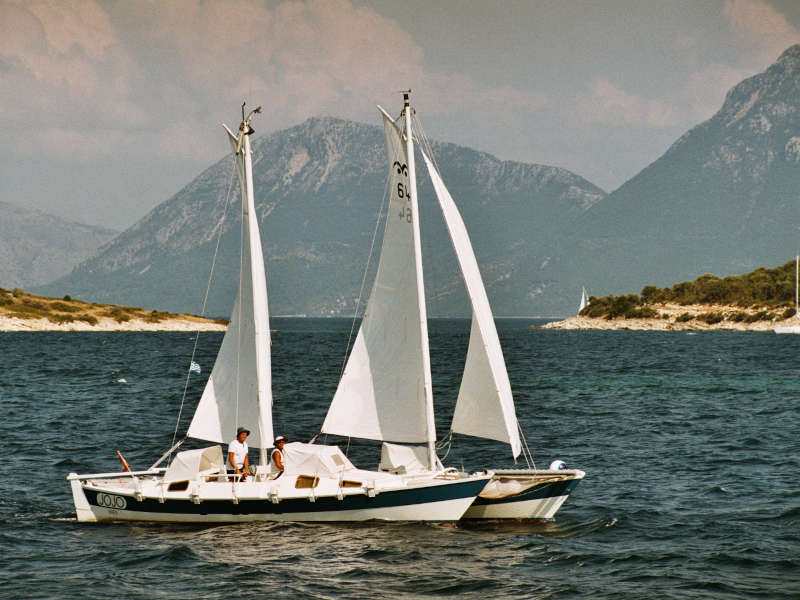 A catamaran called JoJo sailing against a backdrop of mountains
