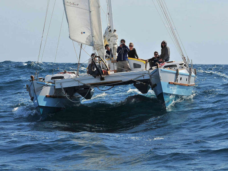 Rear view of a large catamaran sailing away, many people aboard
