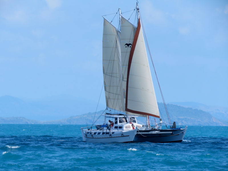 Very large catamaran with all sails up, sailing on a very blue sea