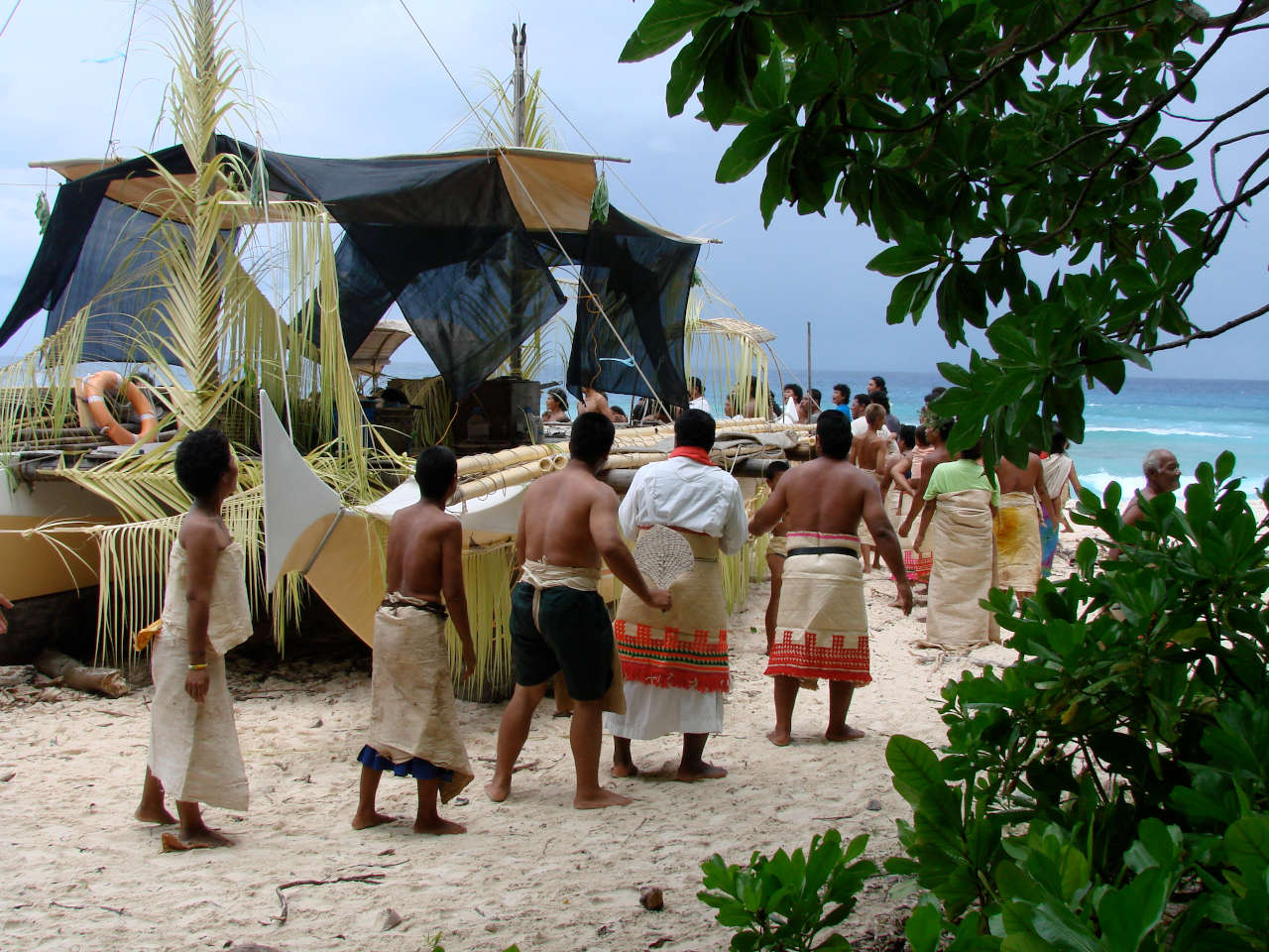 People wearing sarongs walking around a beached double canoe