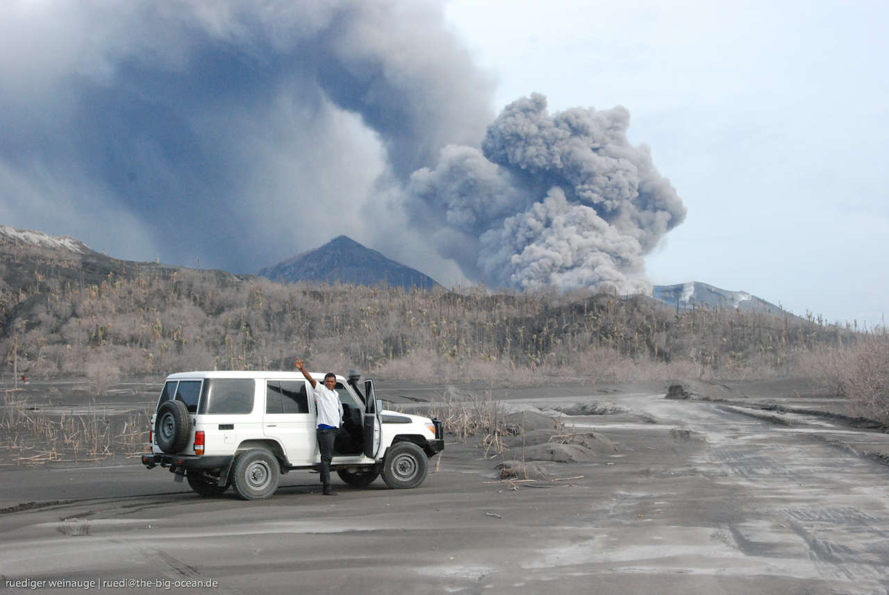 Jeep in front of an erupting volcano in the distance