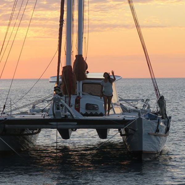 Large catamaran on the water, one woman on deck waving