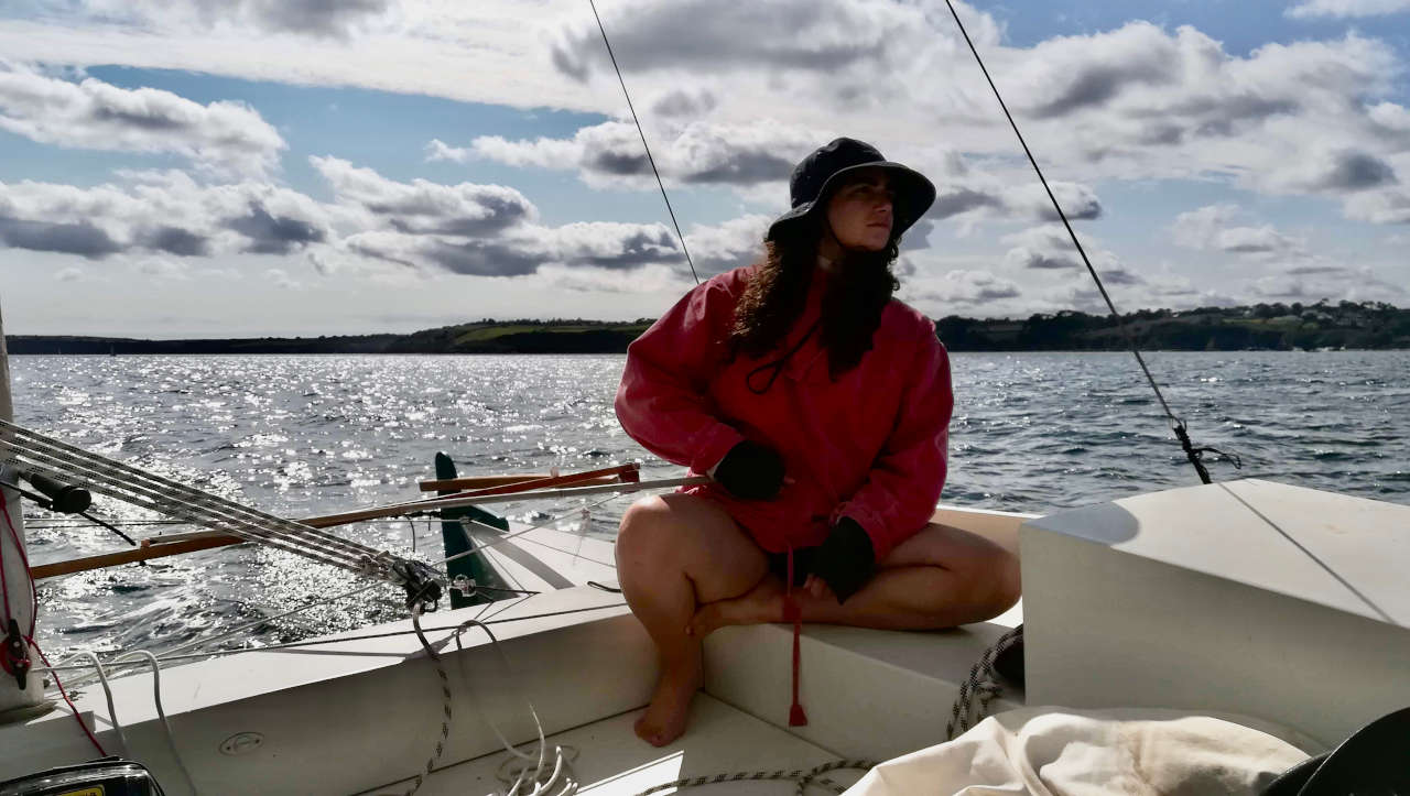 A woman sailing a catamaran, tiller in hand, glistening sea