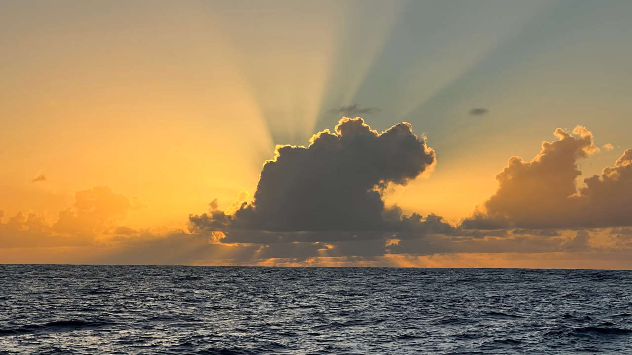 A dramatic sunset over an open sea, edges of large clouds glowing orange