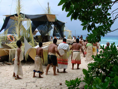 People wearing sarongs walking around a beached double canoe