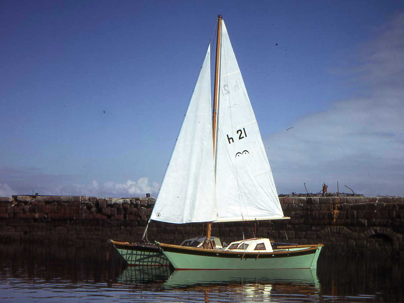 Hinemoa with green hulls and sails up, in a harbour