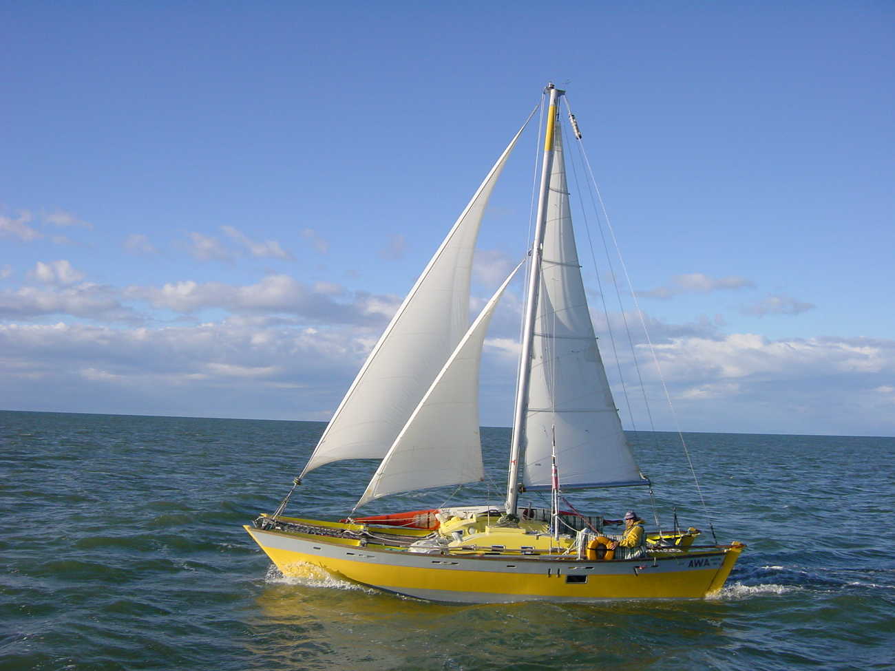 Yellow hulled Tanenui sailing out in the open, one man aboard