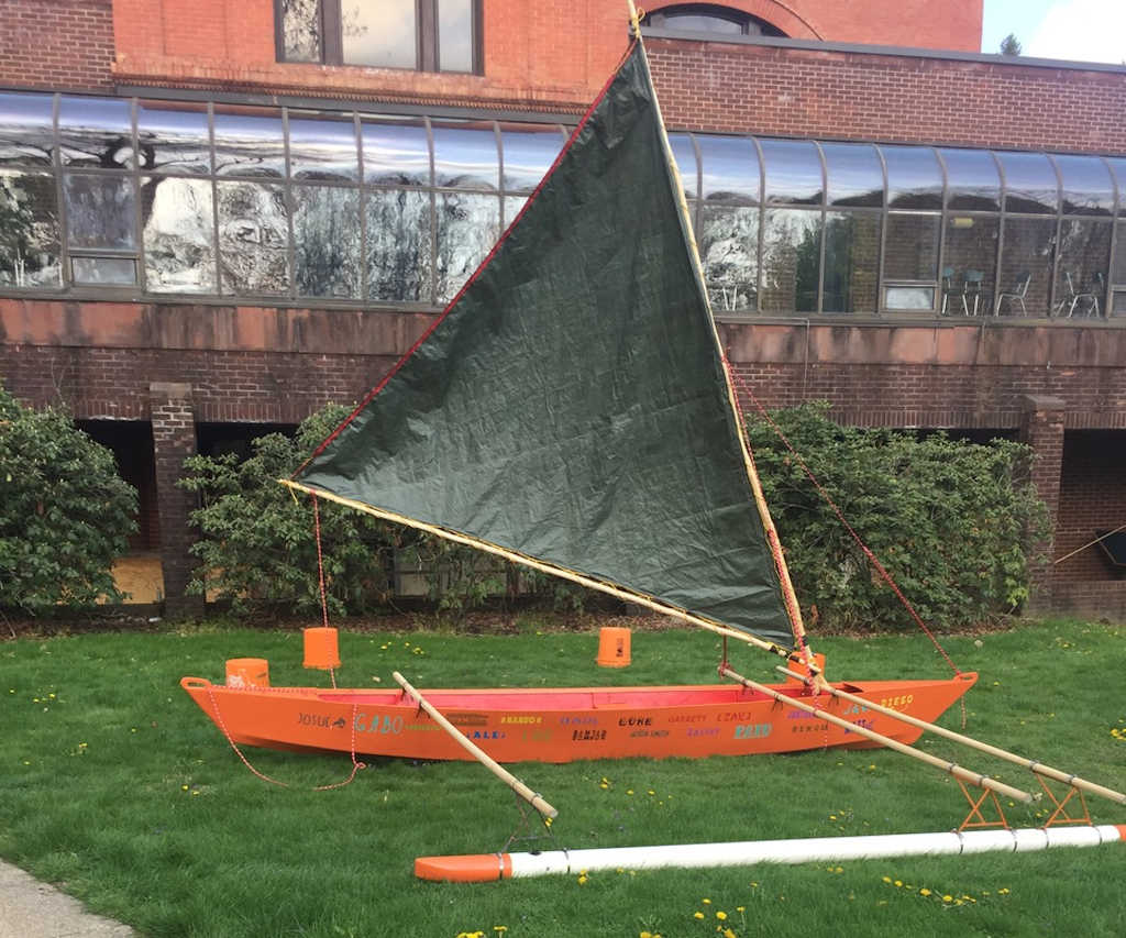 Orange outrigger canoe on the grass with green crabclaw sail up