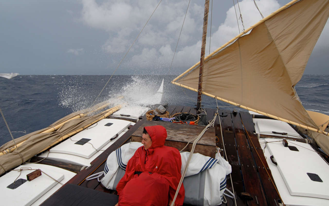 A double canoe on the rough open sea, spray, grey sky, one man on deck