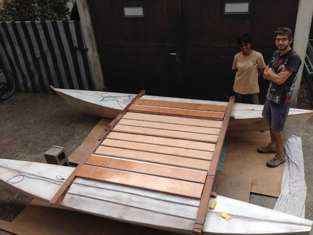 Two people standing next to a partially completed double canoe catamaran