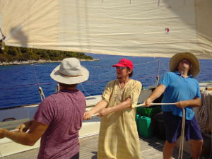 Three crew members pulling a rope to hoist the sails on deck