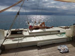 Michael sunbathing on Gaia's deck, mainsail up