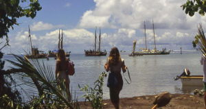 Two woman on beach, looking at group of catamarans on the sea