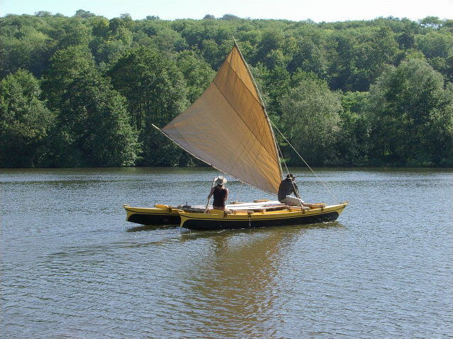 Ethnic style double canoe with crabclaw sail, sailing in a creek