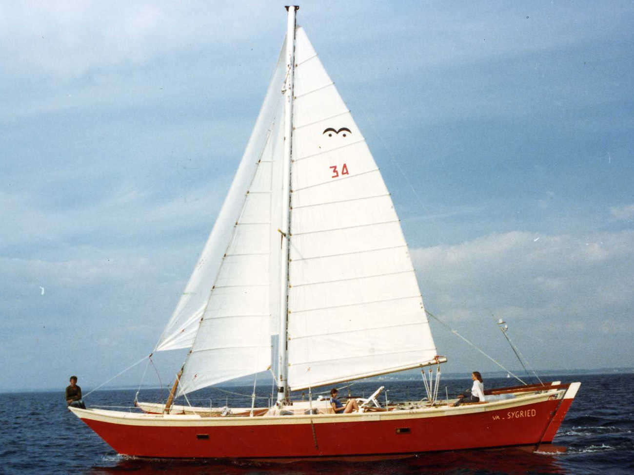 Red hulled Ariki sailing, three people aboard