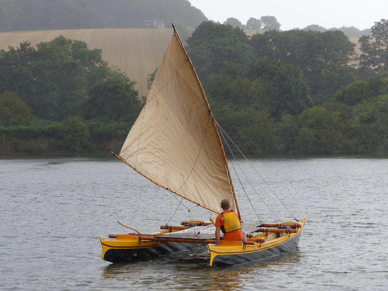 One man sailing a Tahiti wayfarer on a misty creek
