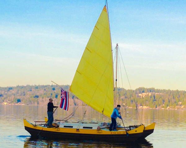 Small double canoe catamaran with yellow sail on the water