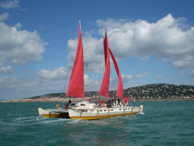Large double canoe catamaran with red sails, cruising the coast
