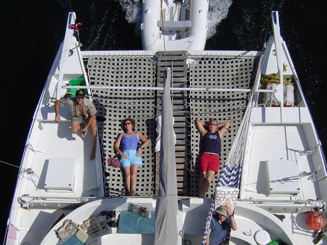 Bird's eye view of a catamaran deck, people lying on the bow trampoline