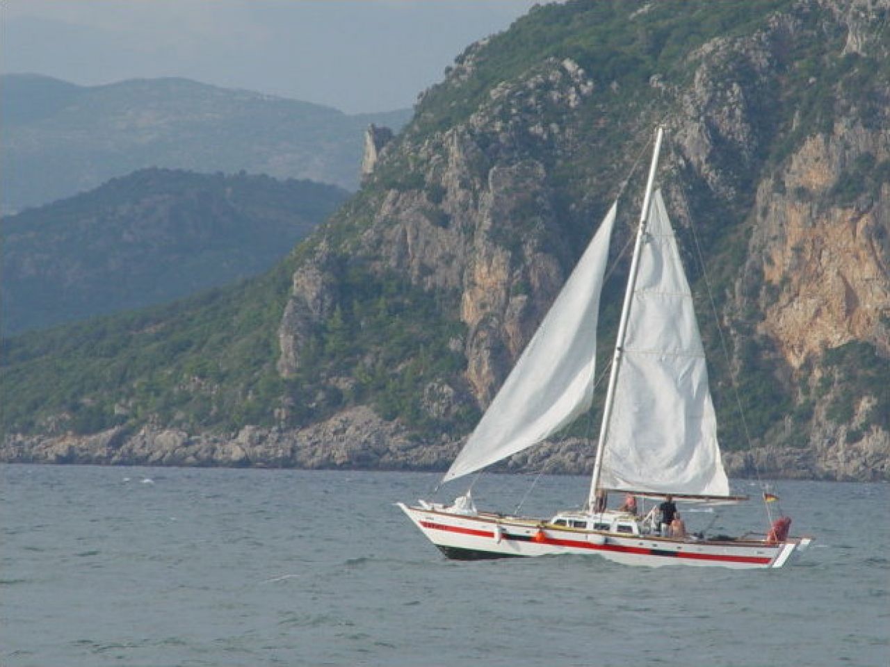 Catamaran saling against a backdrop of dramatic cliffs
