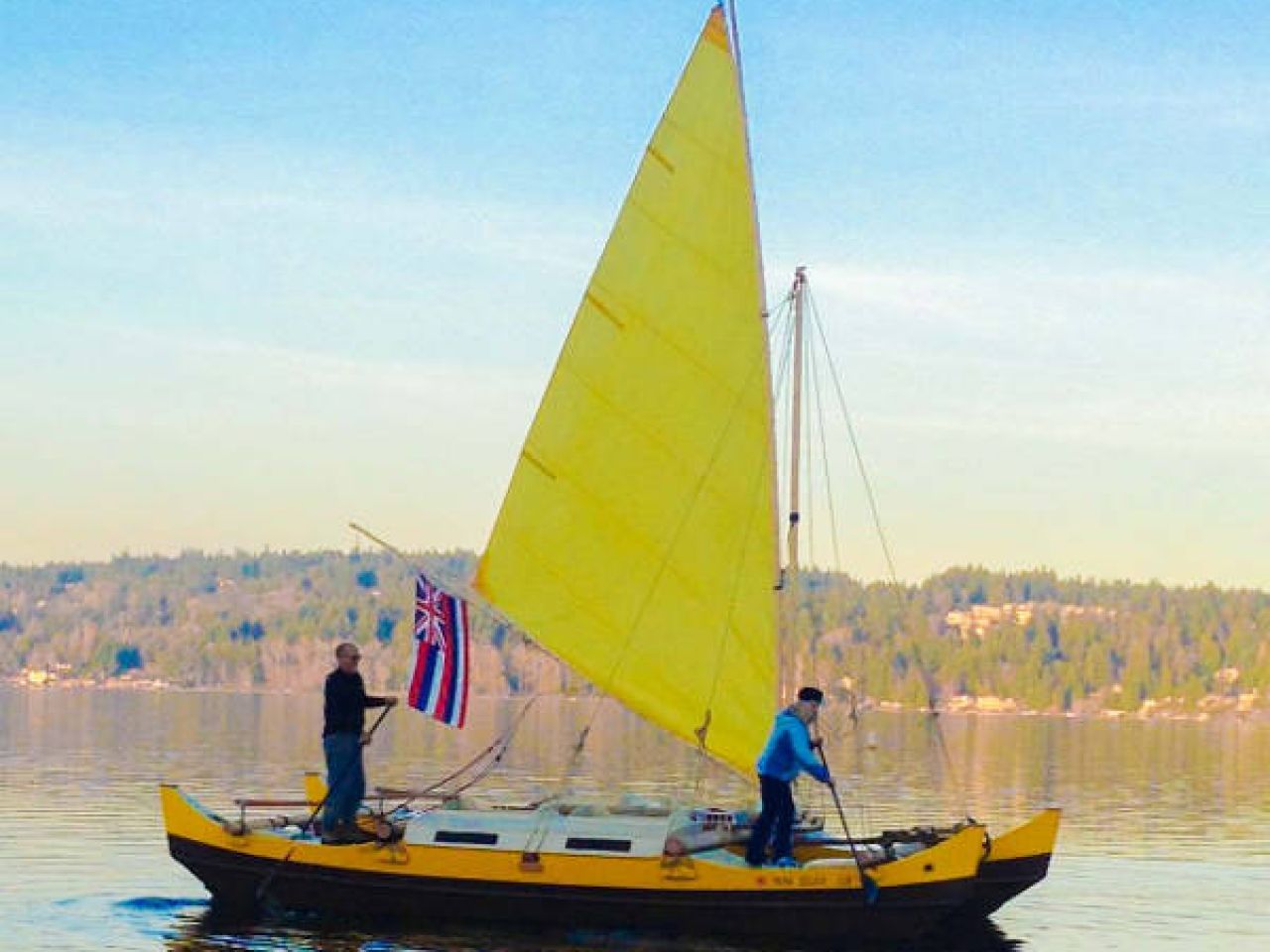 Small double canoe catamaran with yellow sail on the water