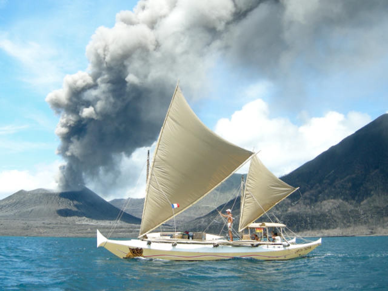 Large ethnic style double canoe sailing against a backdrop of an erupting volcano