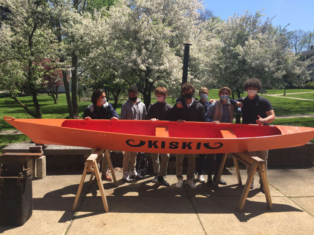 A group of 7 school children with orange outrigger canoe