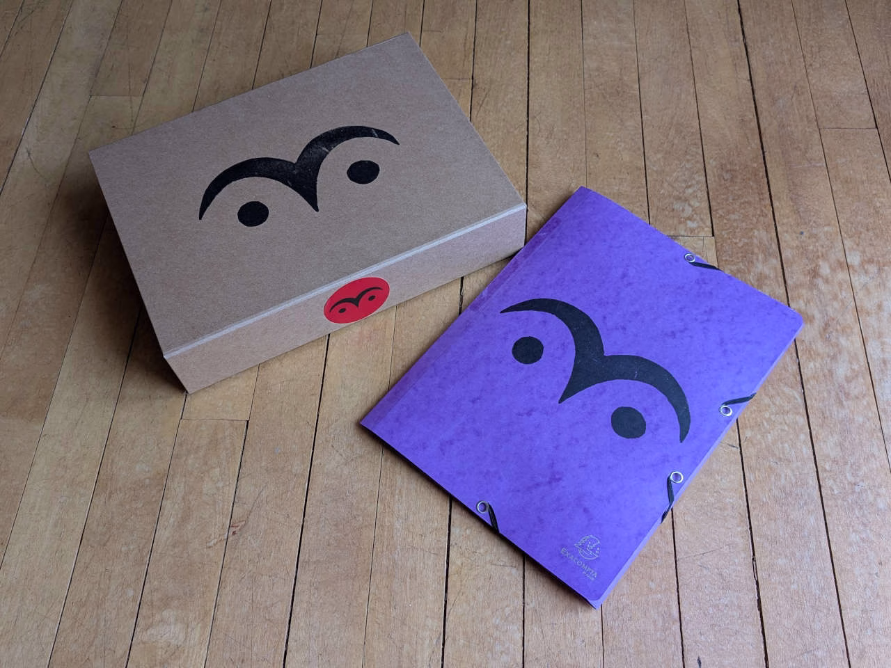 Box and purple elasticated folder, both with owl eye symbol