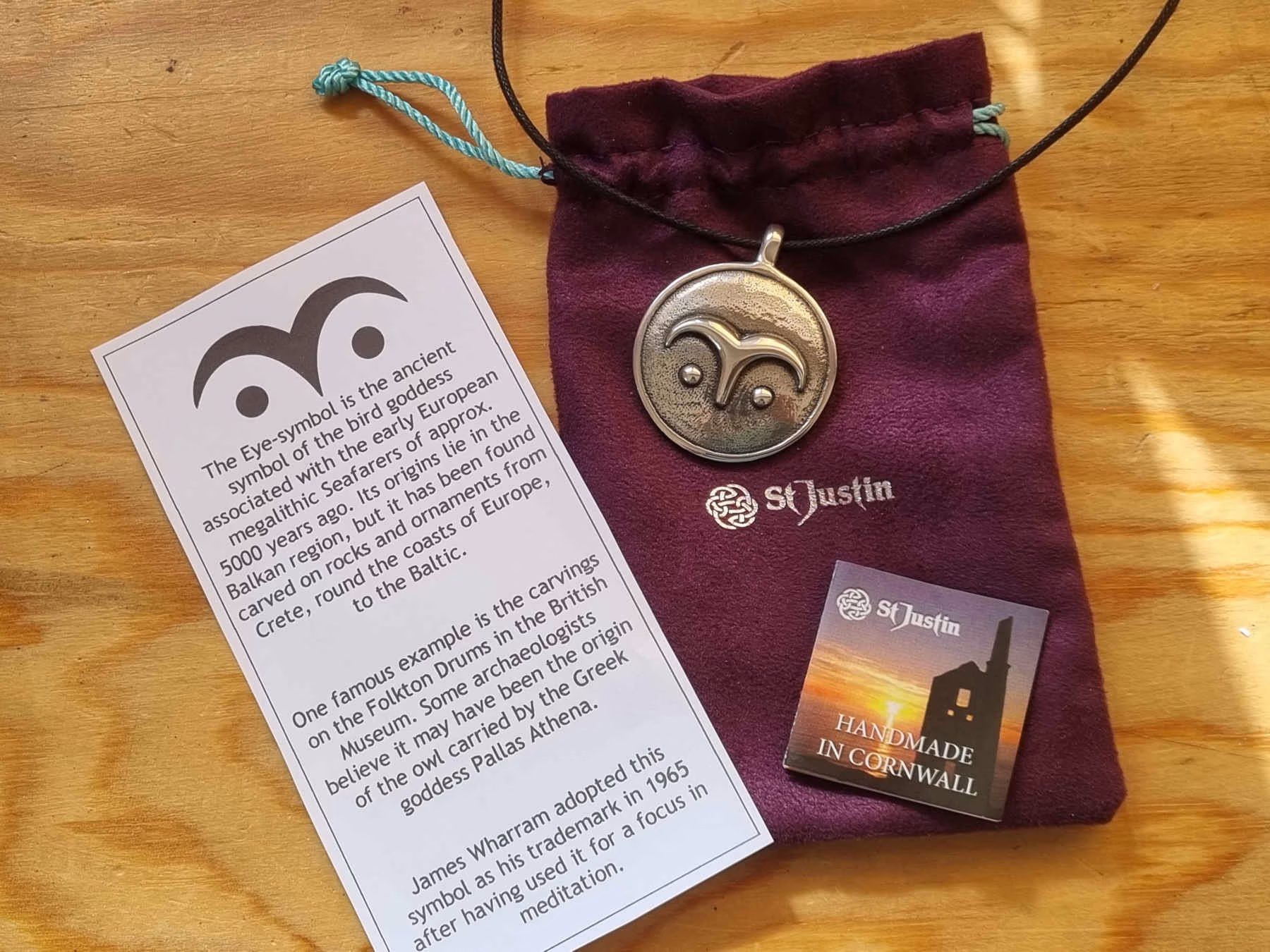 A pewter pendant on a purple velvet pouch, with a description card