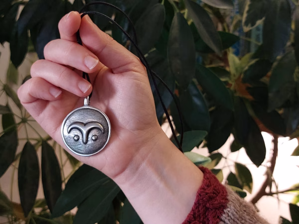 A pewter pendant with owl eyes engraved on it